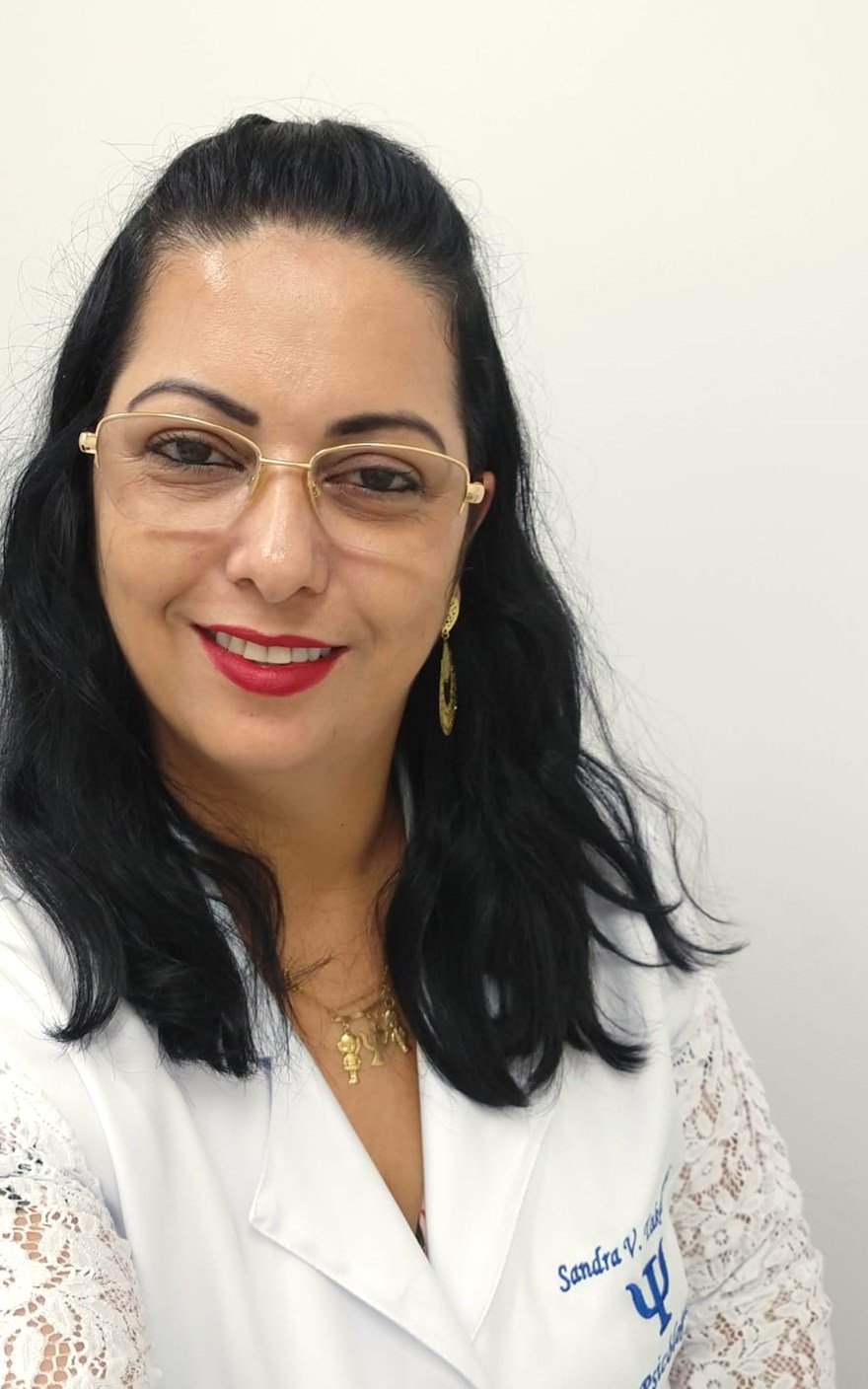 Sandra Suguiura Mota, psicóloga CRP 14/2545, sorrindo, de jaleco branco em seu consultório